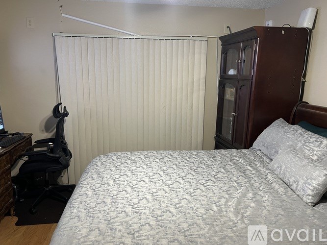 A bedroom with a bed, a desk with a computer, and a cabinet.