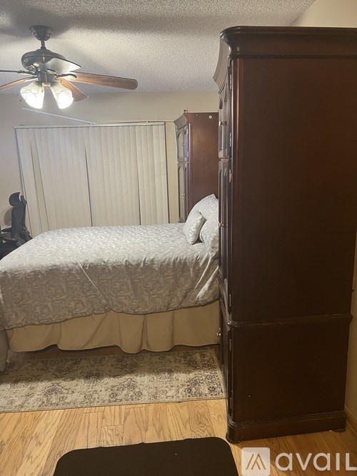 A bedroom with a bed, a ceiling fan, and a wooden armoire.
