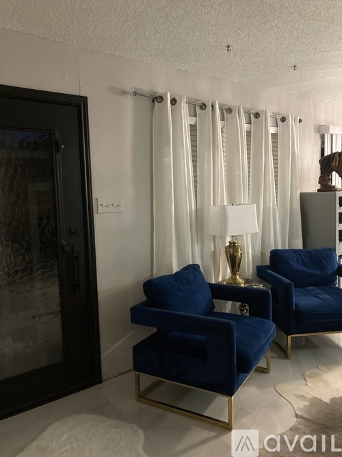 Two blue chairs with gold legs and a table with a vase on it.