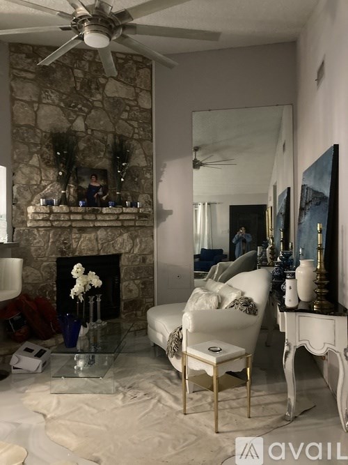 A living room with a stone fireplace and a white chair.