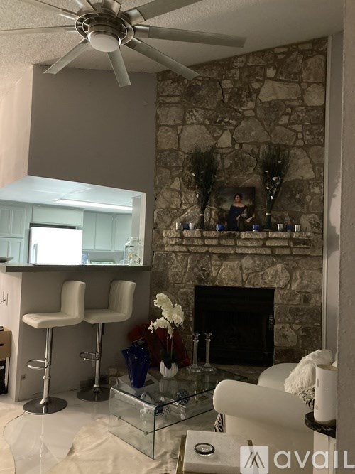 A living room with a stone fireplace and a ceiling fan.