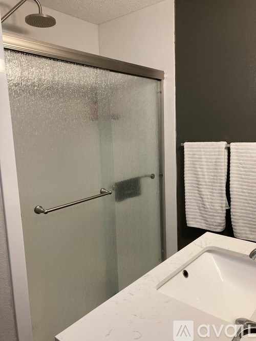 A shower with a glass door and a white sink.