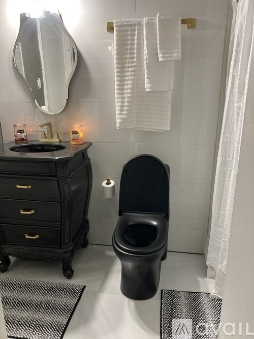 A black toilet in a bathroom with a white towel hanging on the wall.