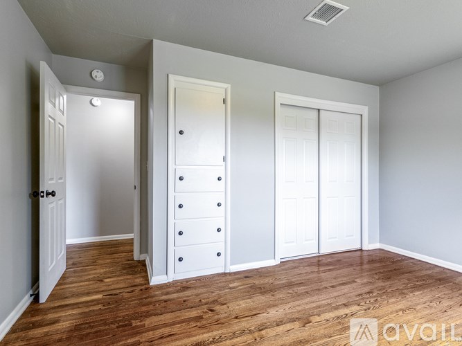 A room with a white door, a white wardrobe with drawers, and a wooden floor.