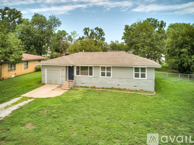 A house with a brown roof and a grey siding is surrounded by a green lawn and trees.