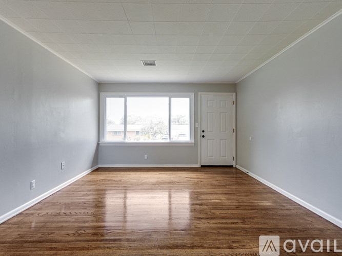 A room with wooden floors and white walls, with a window and a door.