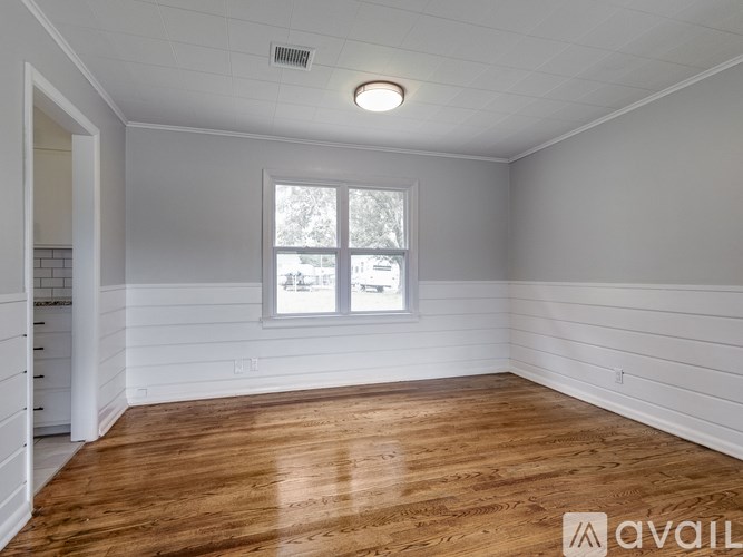 A room with wooden flooring and a window with a view of trees and a building outside.