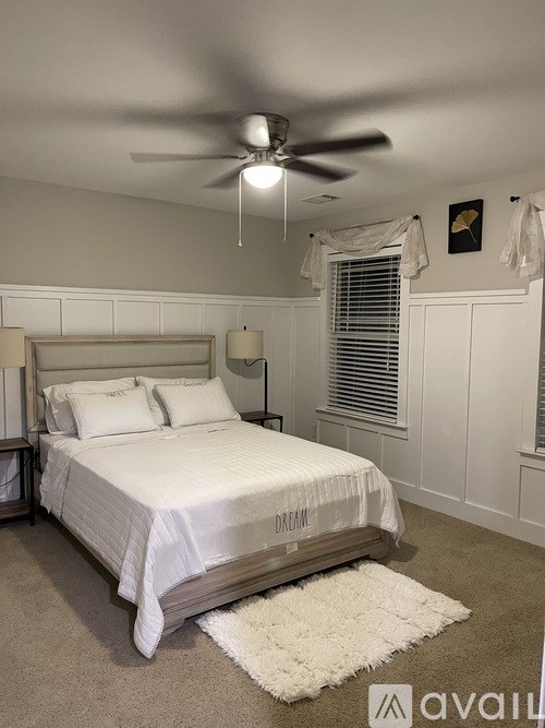 A white bed with a white comforter and pillows in a room with a ceiling fan.