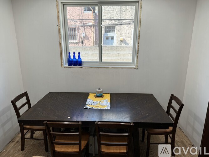 A table with chairs and a window with a view of a building and blue bottles on the windowsill.