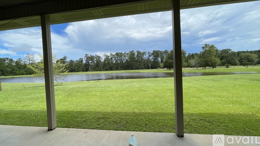 A view from a covered patio looking out to a grassy field and a lake.