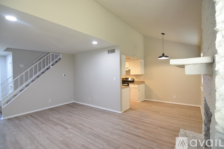 A spacious room with wooden flooring and a staircase on the left side.