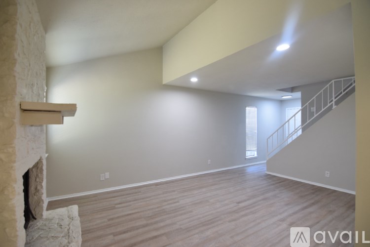 A spacious room with wooden flooring and a stone fireplace on the left side.