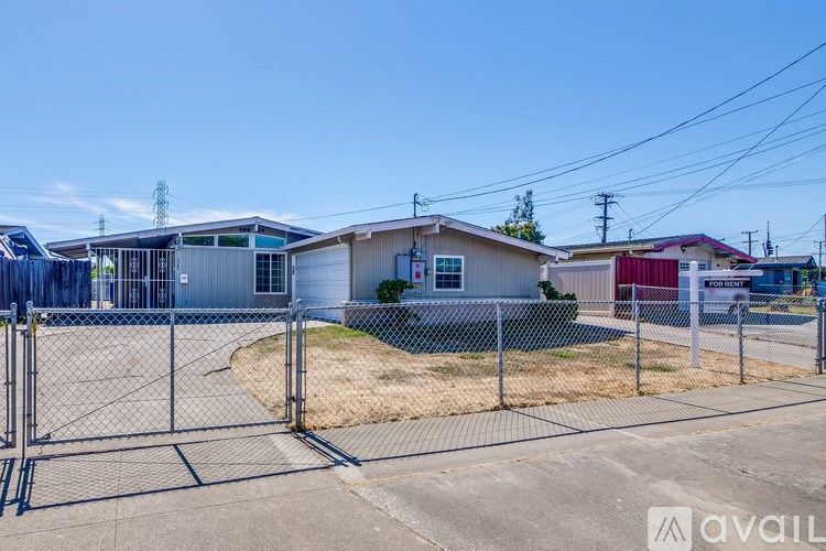 A chain link fence surrounds a vacant lot with a few buildings in the background.