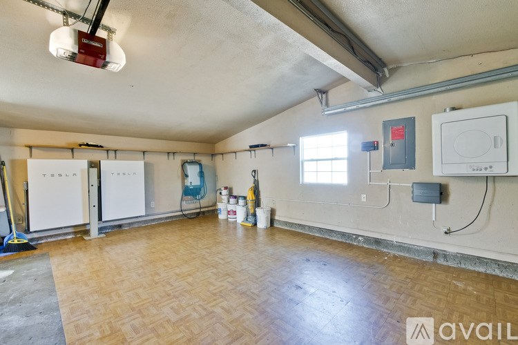 A room with a Tesla branded fridge and a vacuum cleaner.