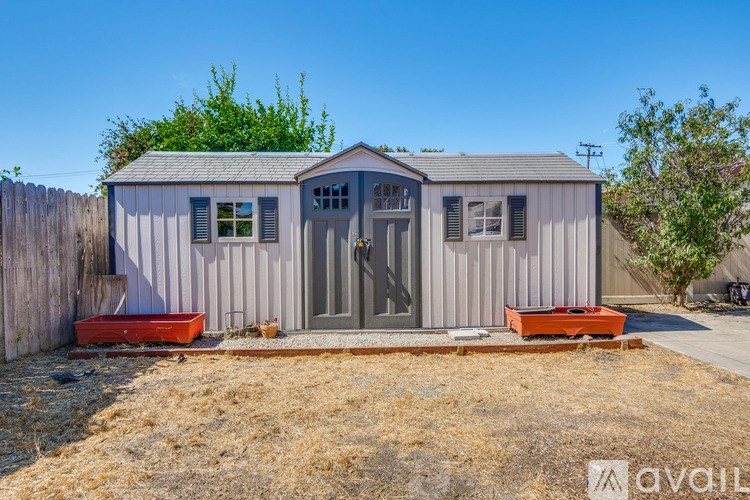 A small house with a grey roof and a grey wall is surrounded by a wooden fence.