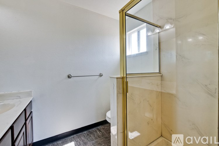 A bathroom with a marble shower and a gold framed mirror.
