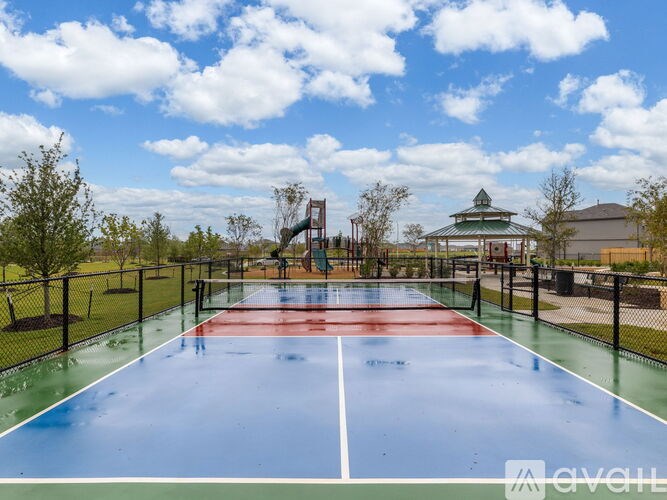 A tennis court with a red and green surface is surrounded by a black fence.