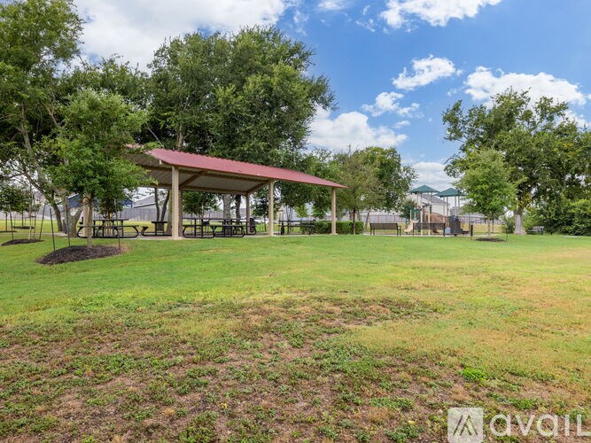 A pavilion with a red roof is surrounded by trees and grass.