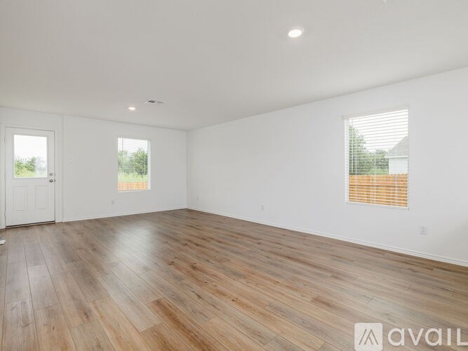 A spacious room with wooden flooring and two windows.