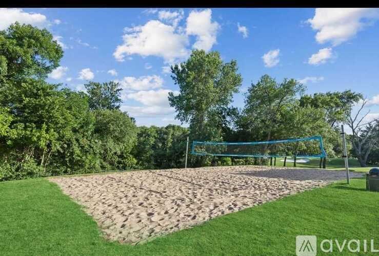 A blue volleyball net stands in the middle of a sandy area.