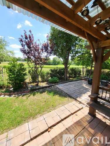A wooden pergola overlooks a patio with a view of a grassy field.