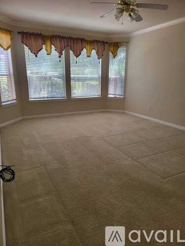 A room with a ceiling fan and windows covered with curtains.