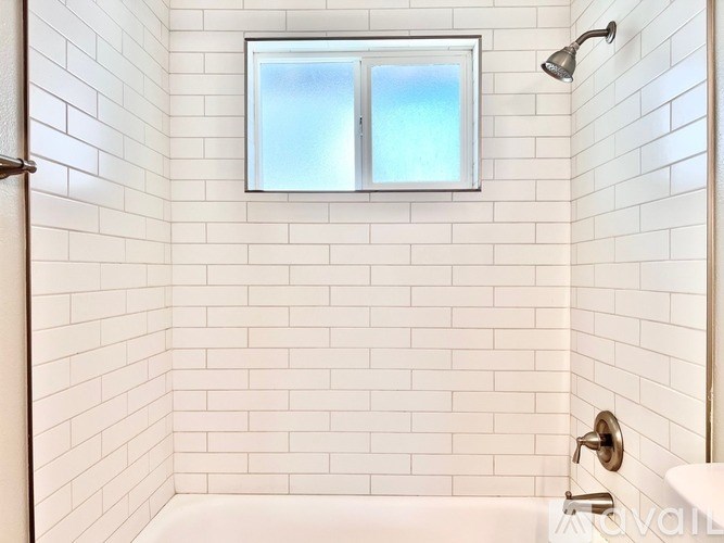 A white tiled bathroom with a window and a bathtub.
