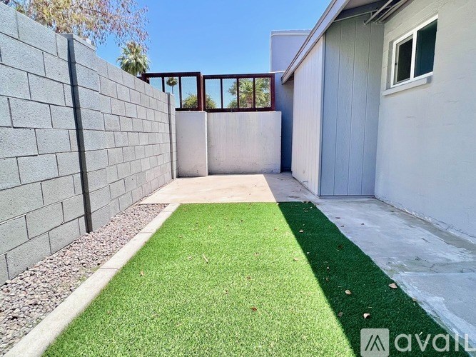 A backyard with a green artificial turf and a grey wall.