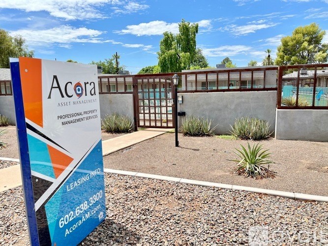 A sign for Acora Asset Management in front of a fence.