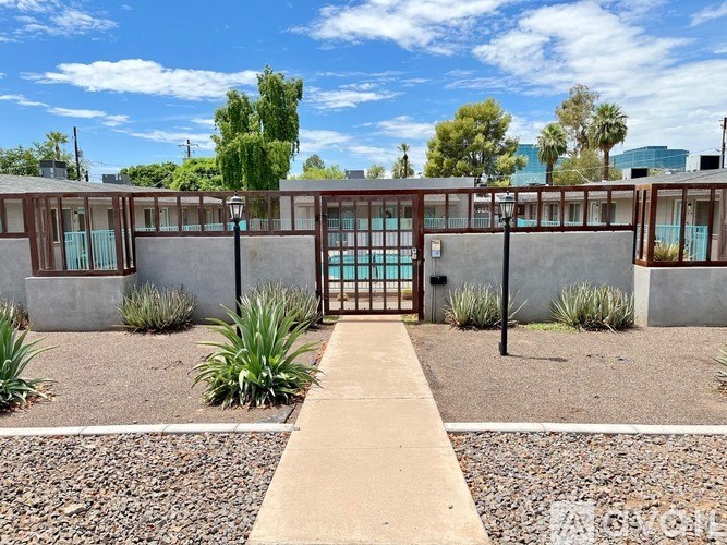 The image shows a concrete building with a metal gate in the foreground and a clear blue sky above.