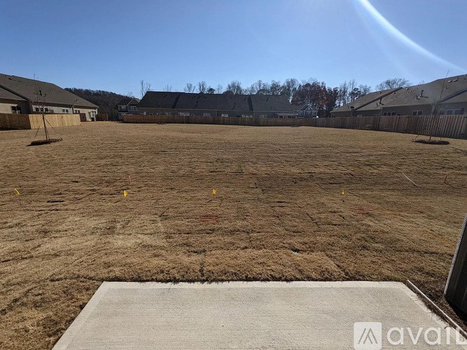 A large, empty field with a clear sky and a few buildings in the distance.
