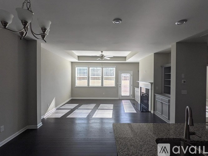 A spacious living room with a chandelier, a ceiling fan, and a large window with a view of the city.