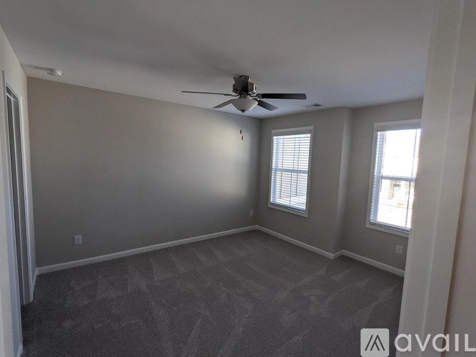 A spacious room with a ceiling fan and two windows.