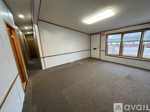 A room with a carpeted floor, a door, and a window with a view of the outside.
