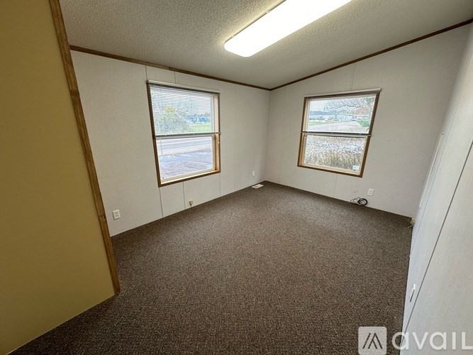 A room with carpeted floor and two windows.