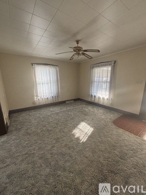 A room with a ceiling fan and two windows.