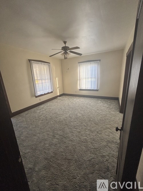 A carpeted room with a ceiling fan and two windows.