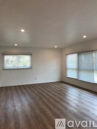 A room with wooden flooring and two windows with blinds.