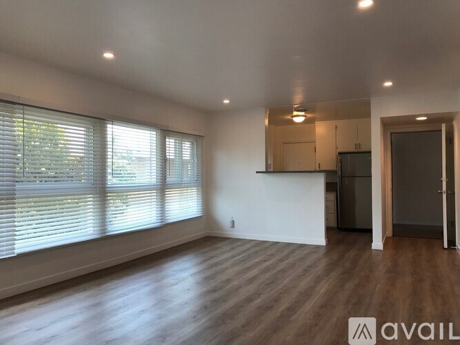 A spacious room with wooden floors and a kitchen area in the background.