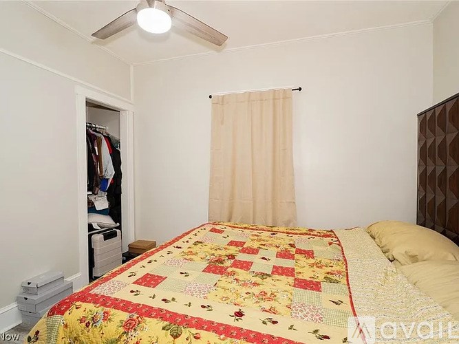 A bedroom with a bed covered in a quilt and a closet with clothes.