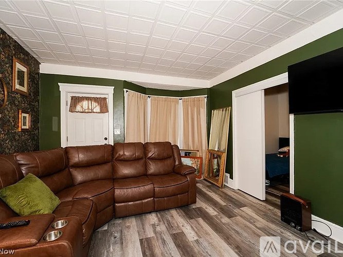 A brown leather couch with a remote control on it in a room with green walls.