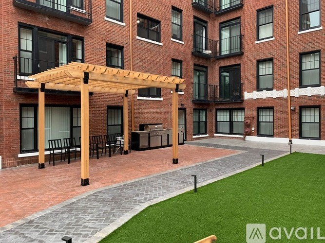 A patio area with a pergola and seating area in front of a brick building.