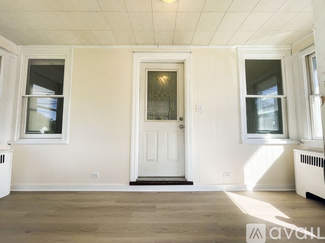 A white door with a glass window is in the middle of a room with white walls and wooden flooring.