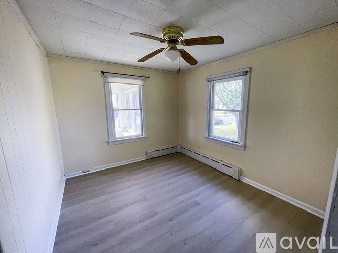 A room with a ceiling fan and two windows.