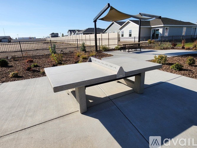 A concrete picnic table is in the foreground of a sunny outdoor area.