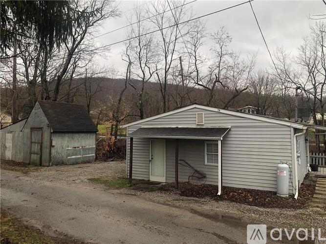 A house with a grey siding and a white door is situated in a rural area.
