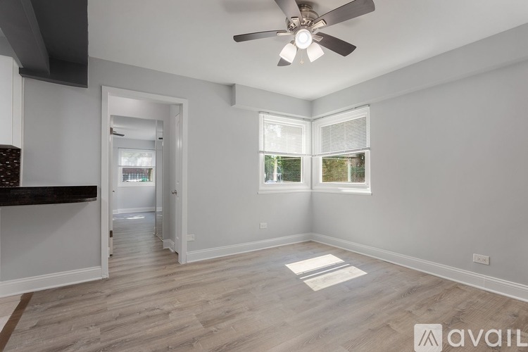 A spacious room with a ceiling fan and light, hardwood flooring, and a window with blinds.
