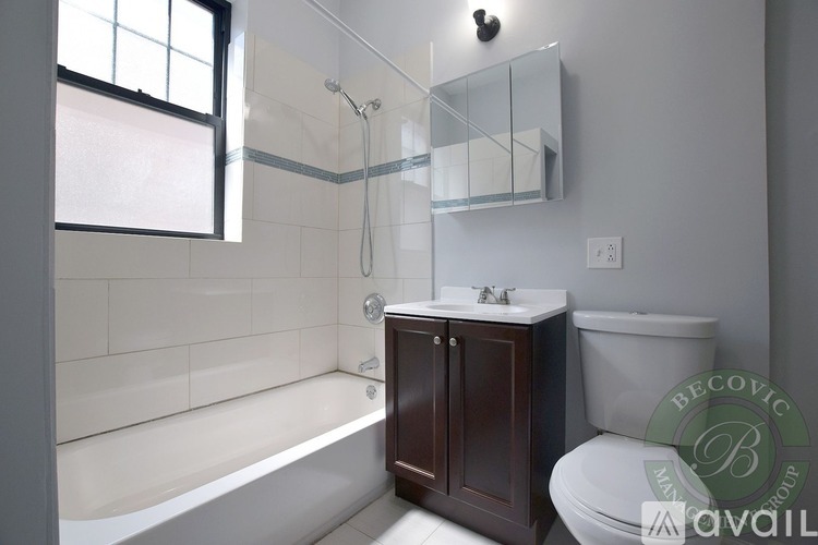 A modern bathroom with a white tub, a white toilet, a sink, and a window.