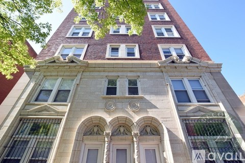 A tall building with a red brick section at the top and a stone facade with arched windows and a balcony.