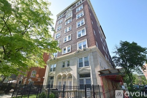 A tall building with a mix of brick and stone facade stands between two trees.